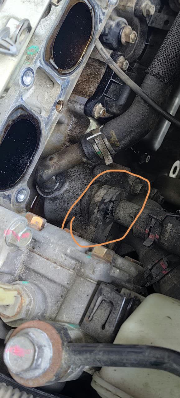 Photo showing the thermostat housing flange location under the intake manifold with visible coolant leak staining