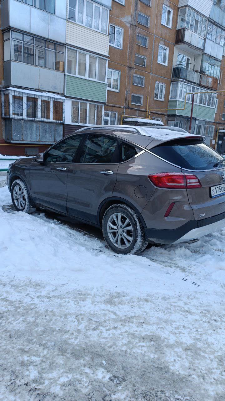 Exterior rear-three-quarter photo of a brown/bronze 2020 X80 parked in a snowy residential courtyard, rear license plate partially visible