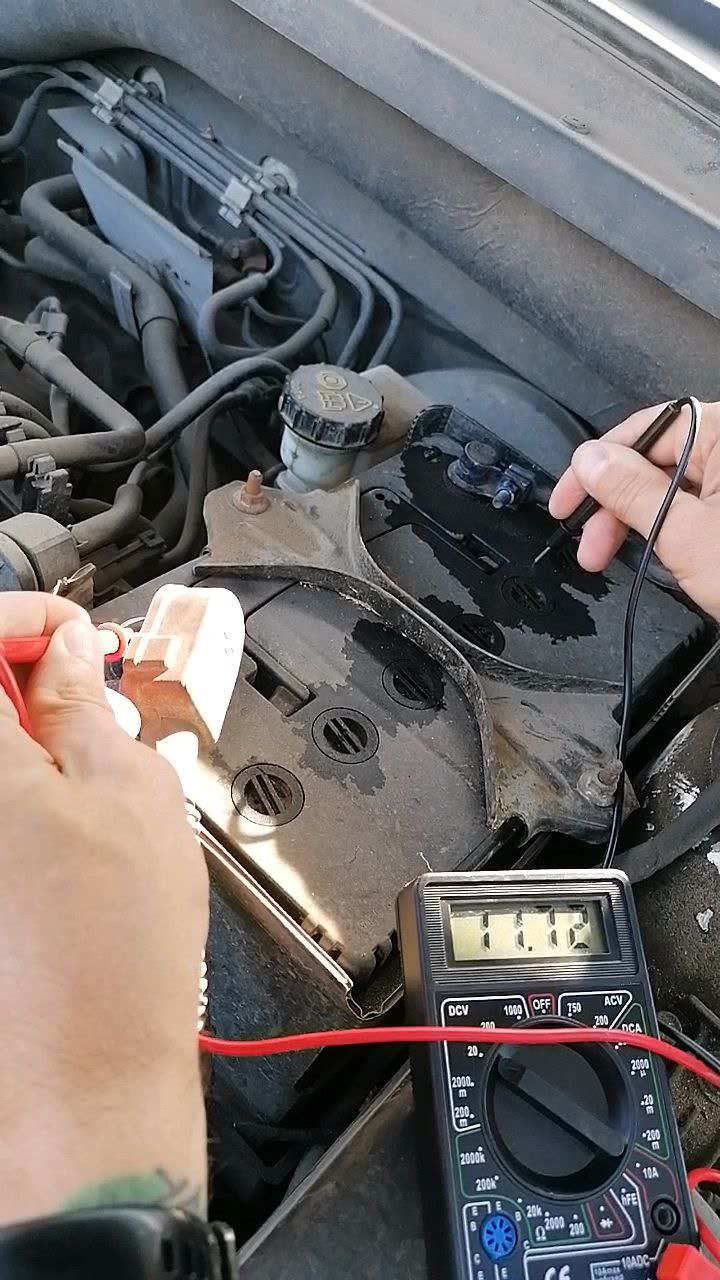 Dirty battery terminal with electrolyte residue, a multimeter measuring the voltage drop across the contaminated surface, and an alcohol wipe used for cleaning