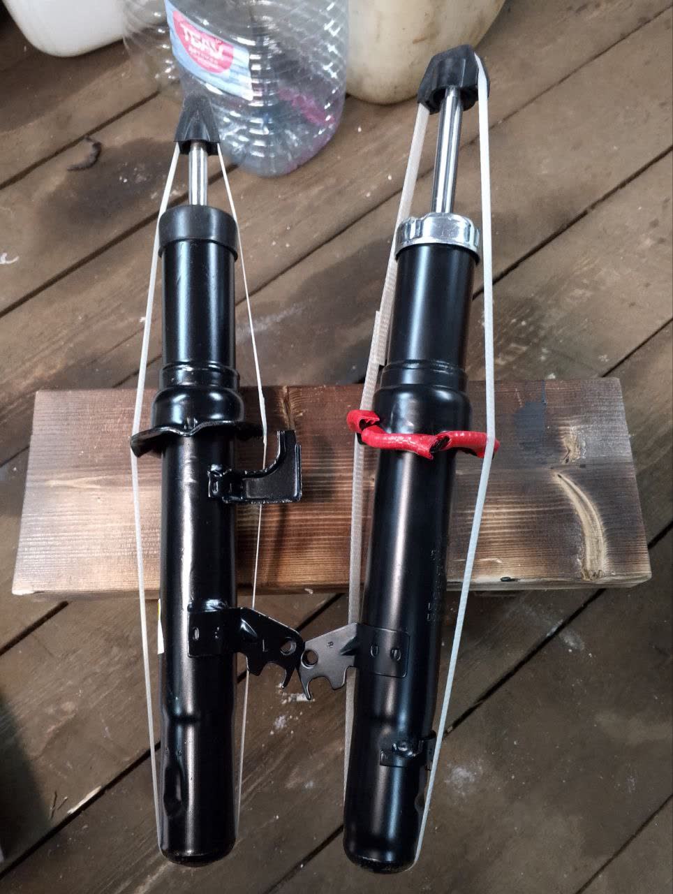 Two shock absorbers side by side showing mismatched hardware finish (left black-painted, right silver/unpainted)