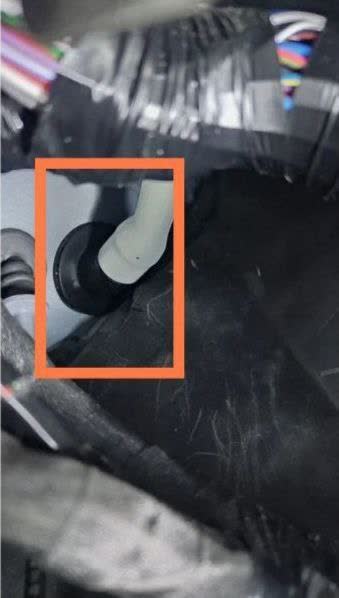 White plastic roof drain fitting with black rubber gasket seal and connection point inside the wheel well area, orange highlight indicating the problem area