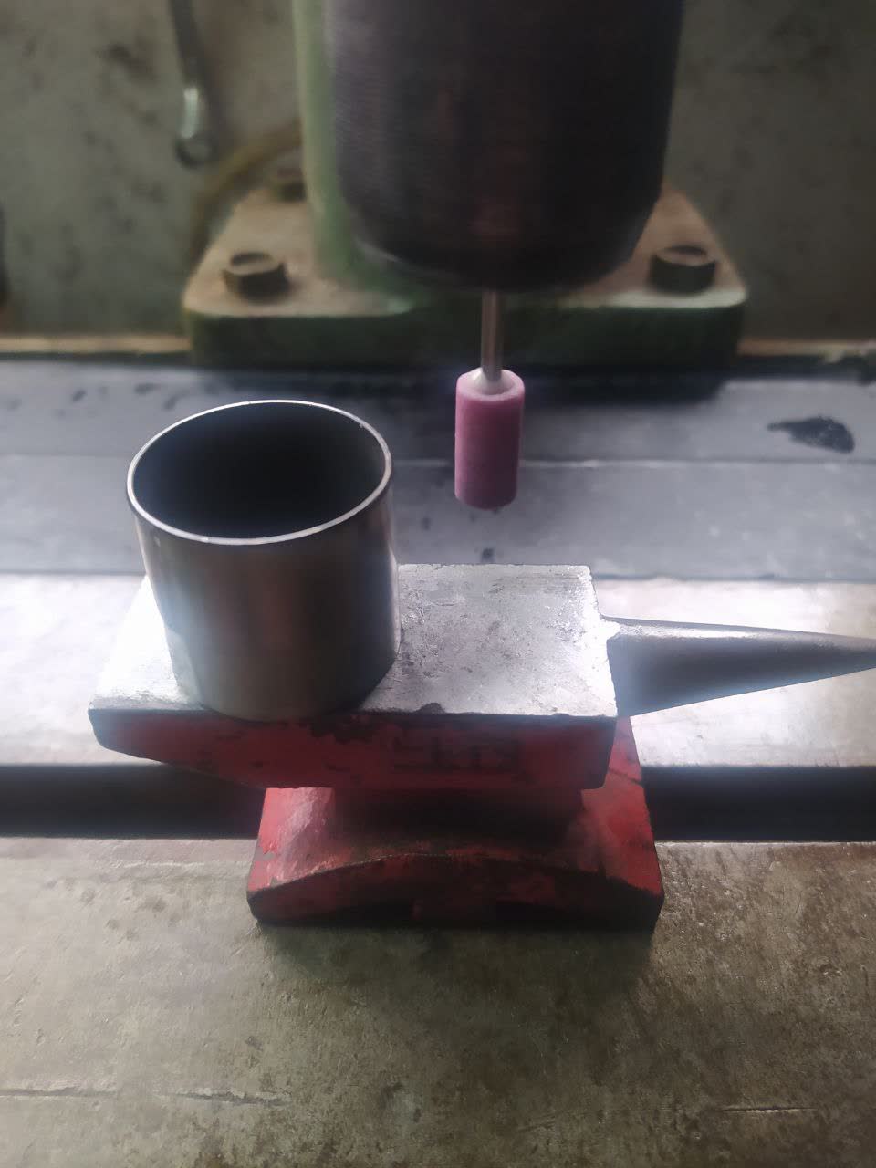 Valve adjustment shim cup on a machining table with grinding/precision finishing setup — demonstrates the manual method of modifying shim cup surfaces