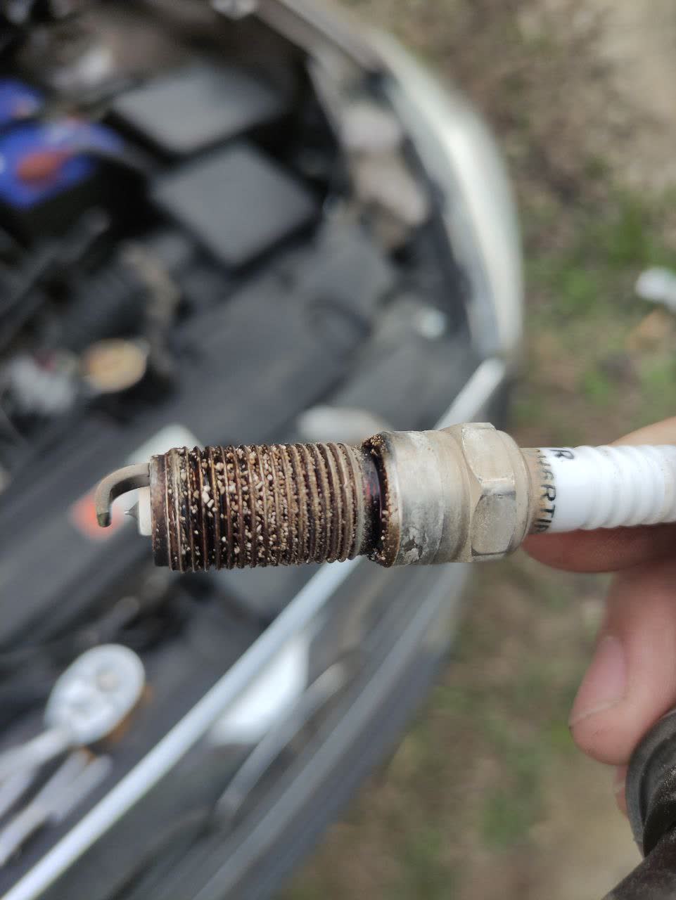 Oxidized spark plug with granular residue on threads, suggesting improper storage or age-related degradation