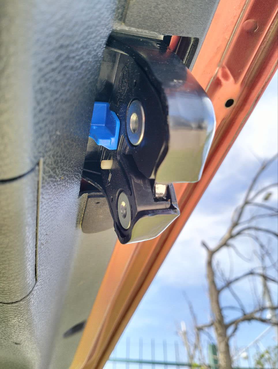 Photo of the trunk latch assembly with a blue actuator component and the mechanical flag lever