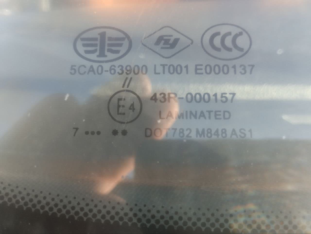 Photo of the windshield showing part-number markings, manufacturing codes, and certification marks