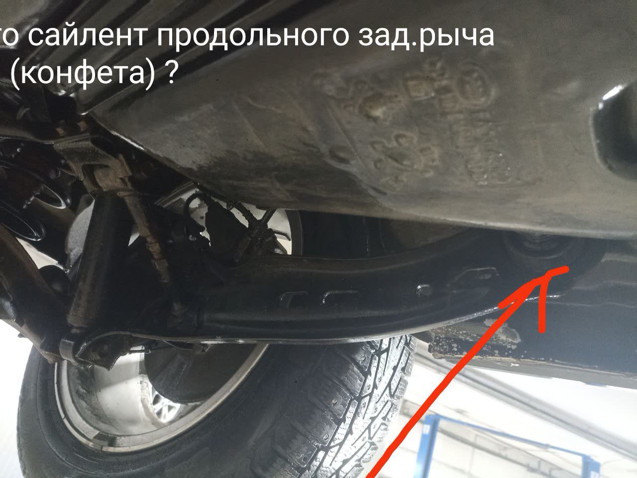 Lower control arm assembly with the bushing location marked by a red arrow
