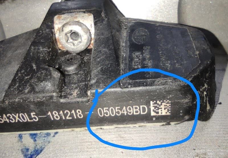 Photo of a TPMS sensor body labelled FS43X0L5-181218-050549BD with a DataMatrix code, the label marked with a blue circle
