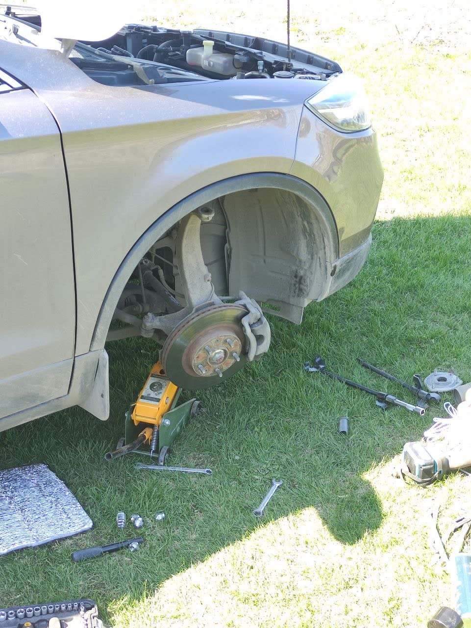 Disassembled front suspension showing brake rotor, damper, and a hand pointing to the repaired/re-pressed area near the upper control arm