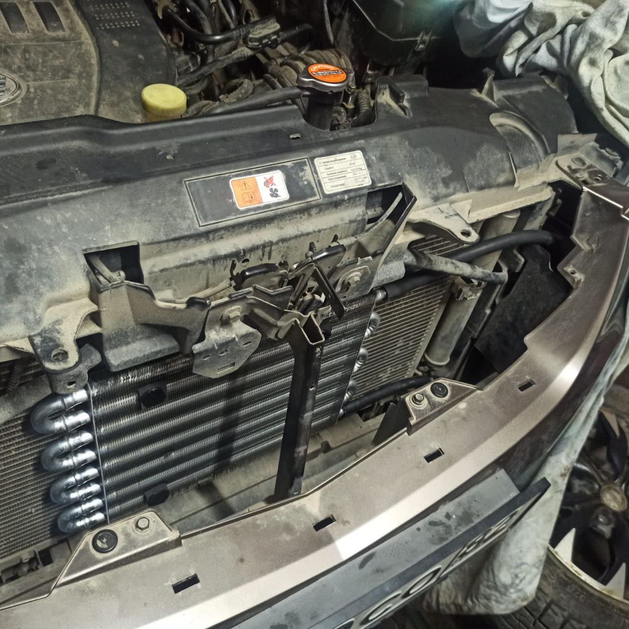 Installed auxiliary AKPP cooler (Hayden OC-1405) with transmission fluid lines connected to both the engine-mounted radiator (left, larger) and the cooler assembly
