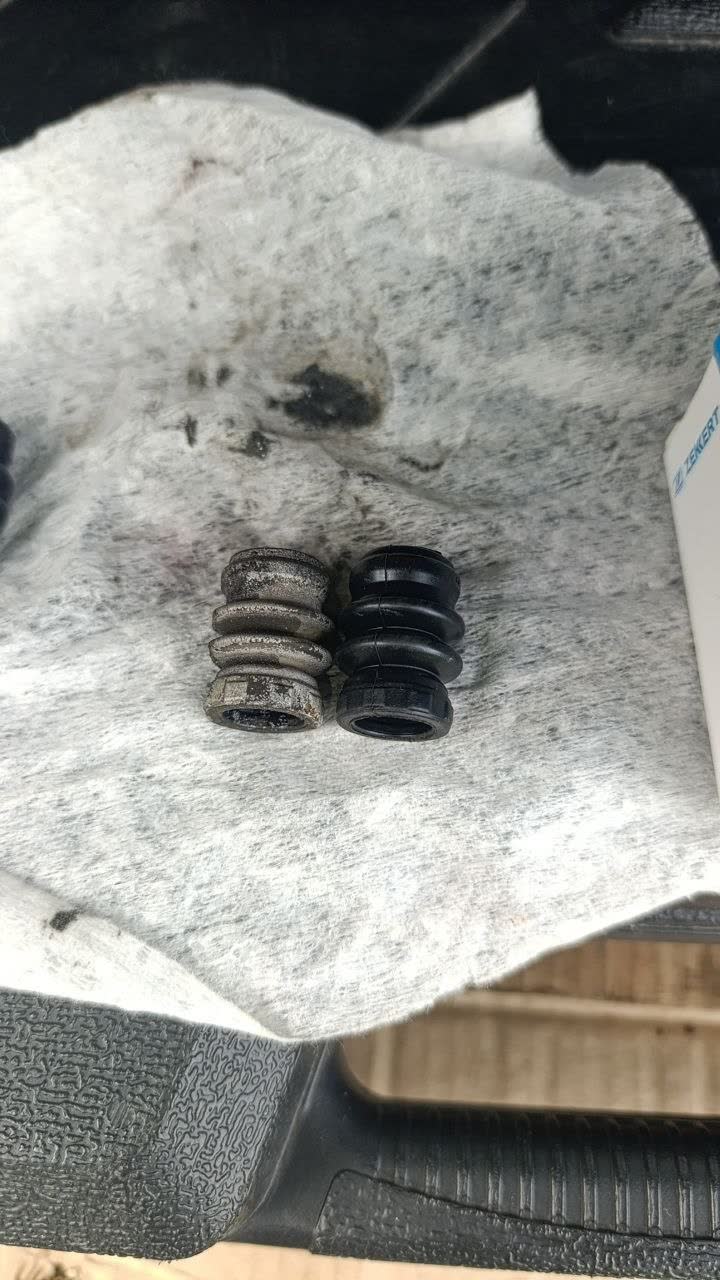 Side-by-side comparison of an old, worn dust boot (grey/corroded, left) next to the confirmed-fitting new replacement boot (black, right), photographed on a shop rag