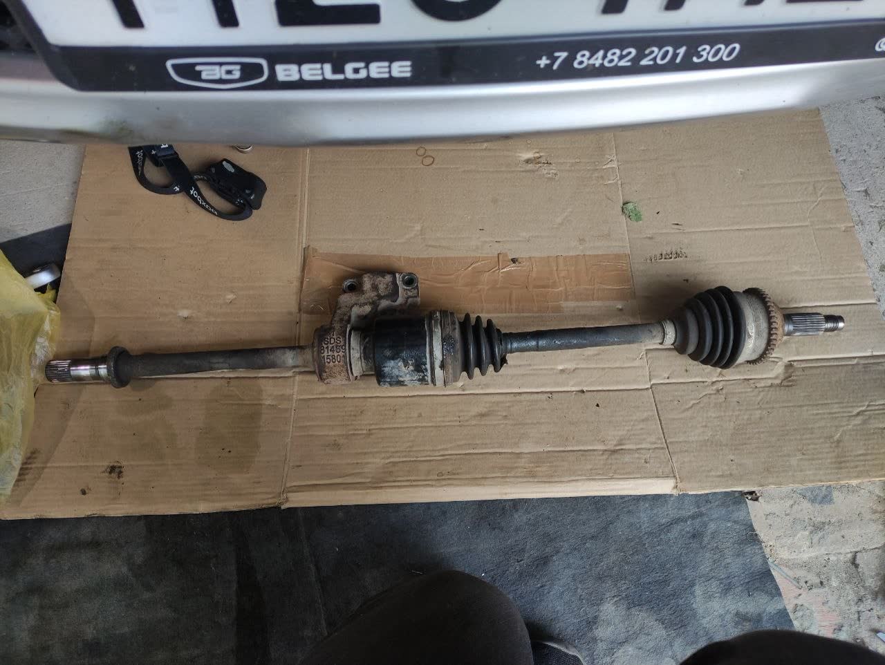 Right drive shaft laid on cardboard: inner joint with a bracket and bolts, splined outer end; the inner joint will not slide off the intermediate shaft because of a circlip