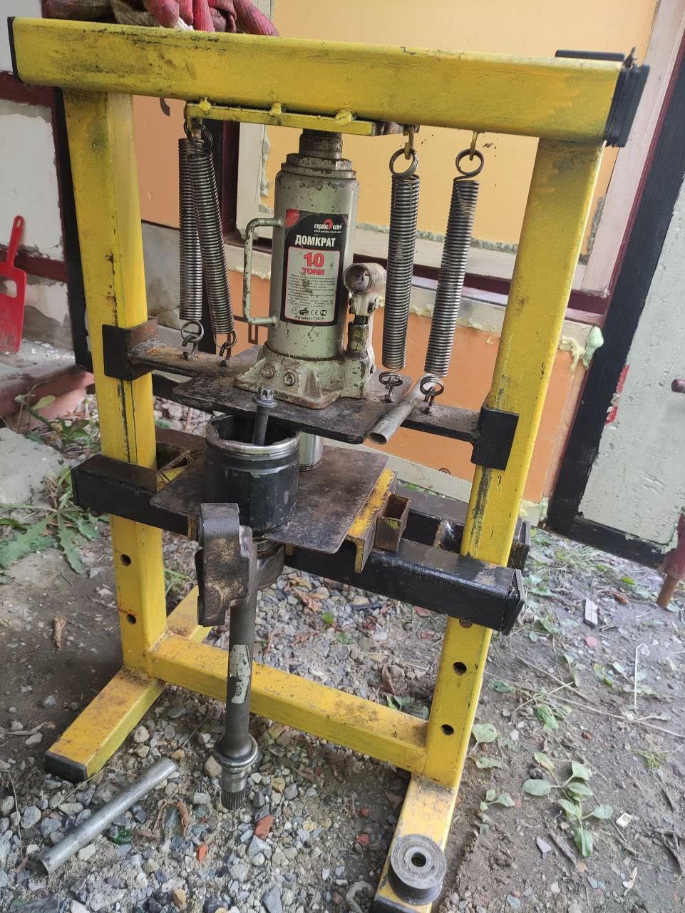 Yellow homemade shop press with a 10-ton bottle jack pressing a shaft in its frame