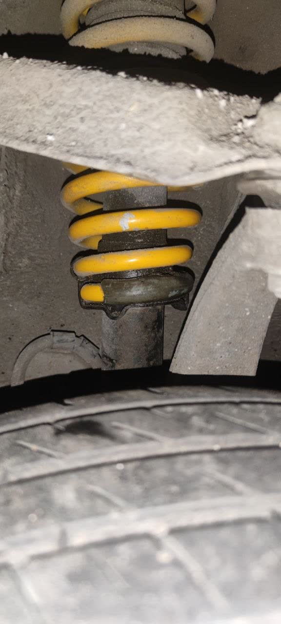 Yellow coil spring seen from inside the wheel arch above a bump stop and a shock (Olga's Suffix springs)