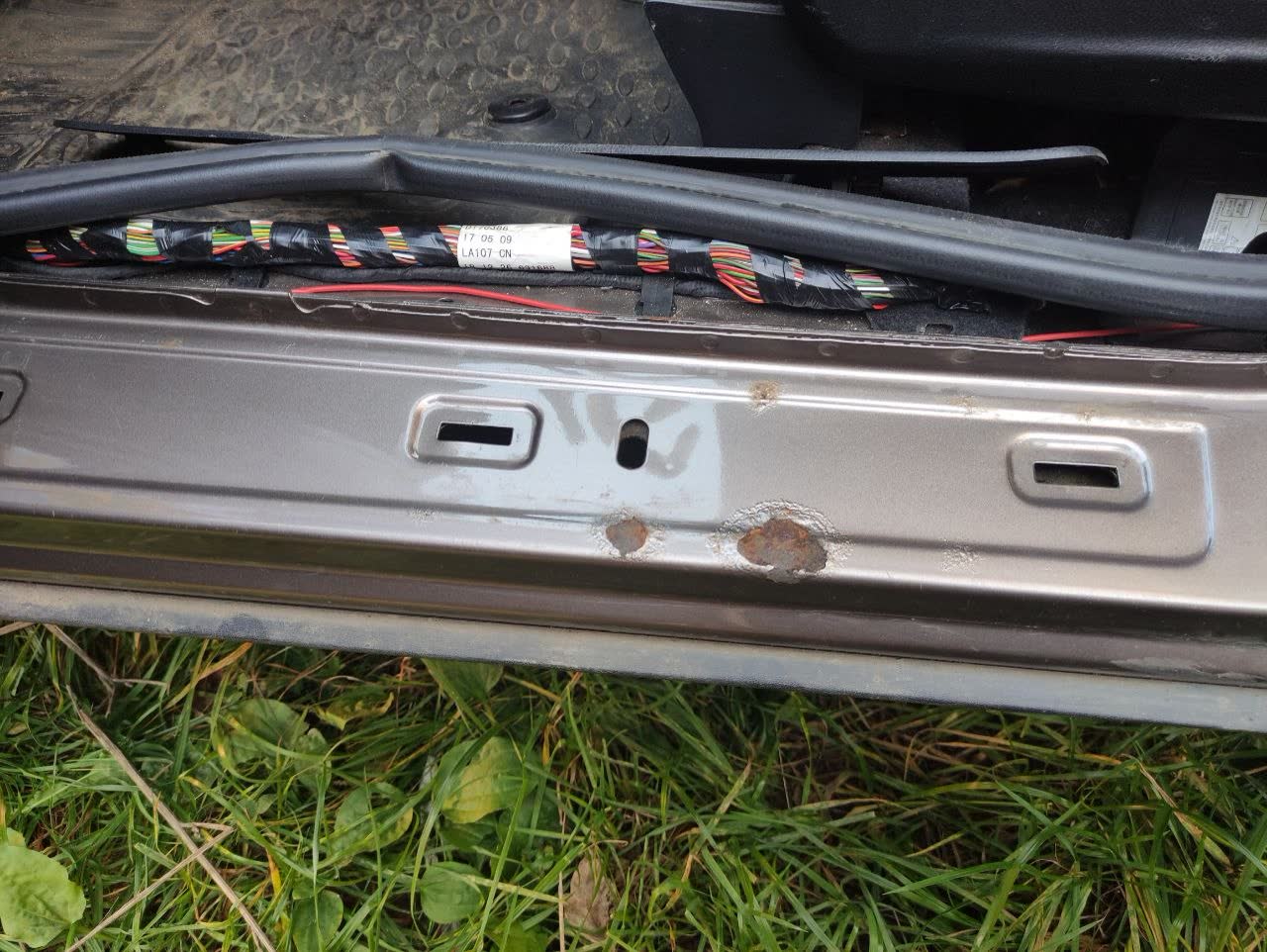 Grey sill with the trim strip removed: several paint blisters and two rust holes around the door-slot cut-outs