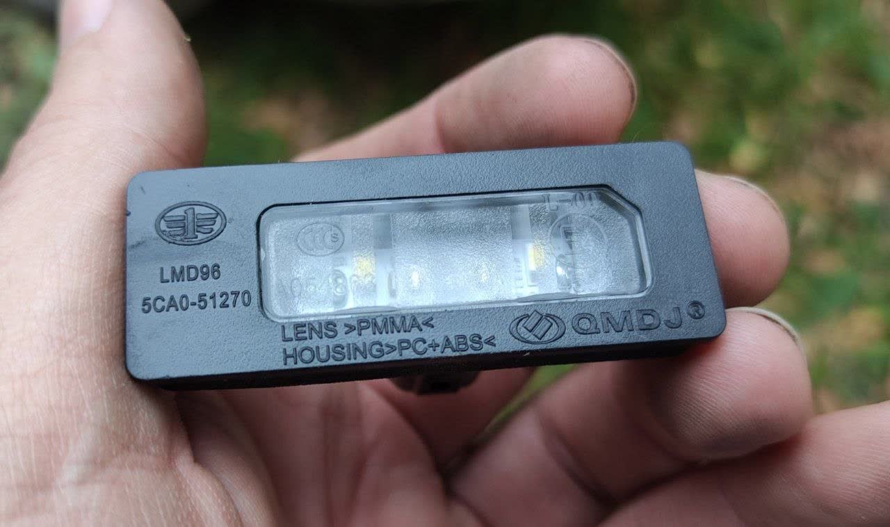 Licence-plate lamp held in hand, embossed 5CA0-51270 and LMD96, FAW logo, QMDJ maker mark, LENS >PMMA<, HOUSING >PC+ABS<