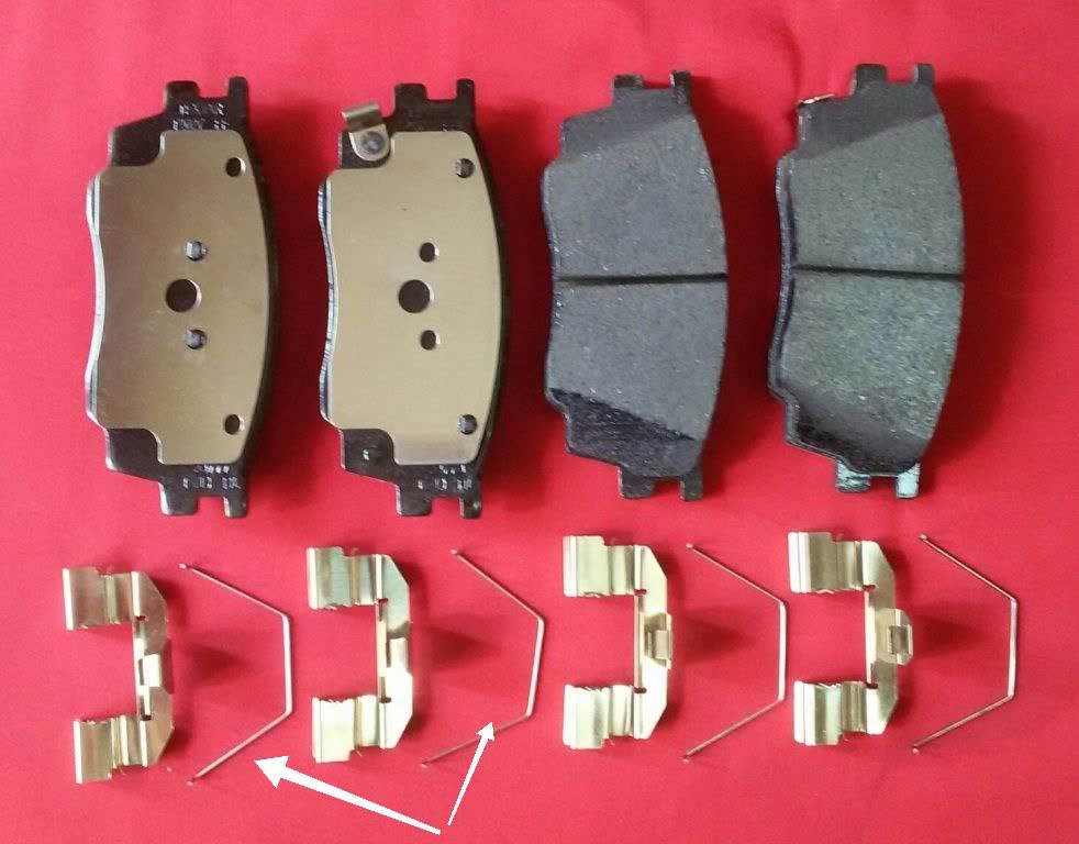 Photo of brake pad assembly with metal spring-tab anti-rattle clips (arrows pointing to individual clips)