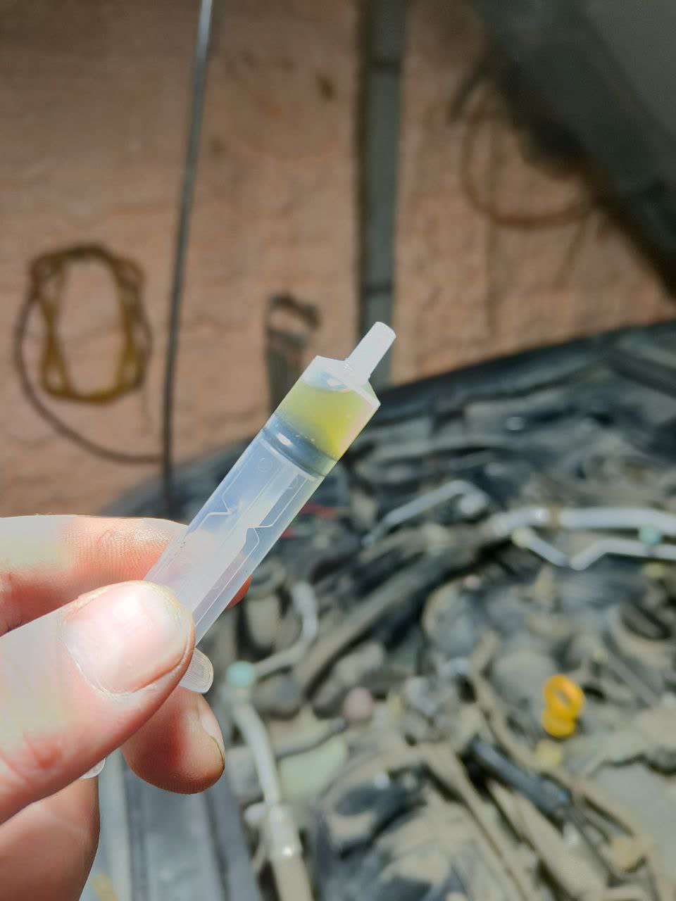 Water/fluid extracted from a spark plug well with a syringe, showing the water intrusion caused by pressure-washing the engine bay