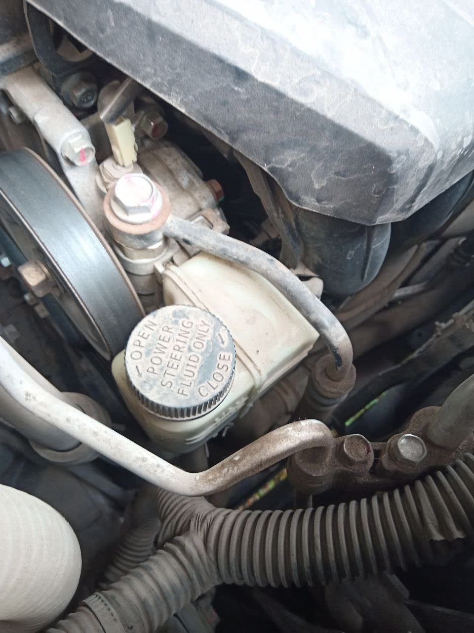 Engine-bay photo showing the power-steering fluid (PSF) fill location and cap label ("POWER STEERING FLUID, CLOSE")